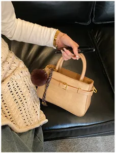Detail of tan bucket bag with woven texture, golden buckle, and faux fur pom-pom charm
