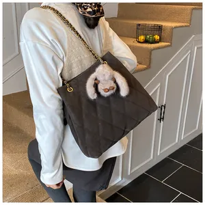 Detail van koffiekleurige gewatteerde tas met gouden ketting en konijn hanger