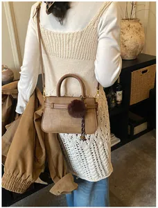 Detailed close-up of brown textured woven bucket bag with pom-pom charm and gold hardware