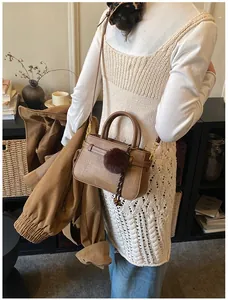 Brown woven bucket bag worn by model with a plush ball charm in a cozy indoor setting