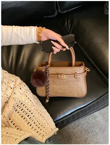 Close-up of brown woven bucket bag with gold hardware and plush charm on a sofa