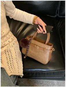 Detail of a brown woven bucket bag with a plush pom-pom and elegant gold hardware