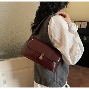 Detail view of burgundy patent leather baguette bag with vintage gold buckle shown underarm