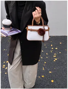 Detail of woven fabric handbag with brown leather trim and decorative fur pom-pom charm