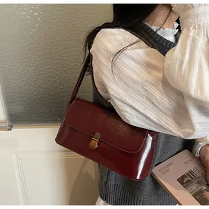 Macro detail of bordeaux red shoulder bag featuring high-gloss leather and gold metal clasp
