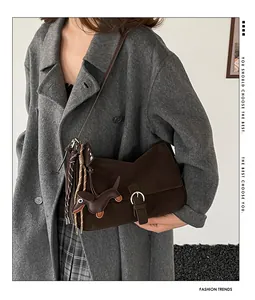 Detail of dark brown suede shoulder bag with unique dachshund dog charm and woven knot strap