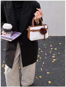 Detail of white fabric bucket bag with brown leather trim and a fluffy pom-pom charm