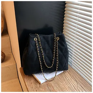 Detail van zwarte gewatteerde shopper met gouden metalen ketting op houten vlak