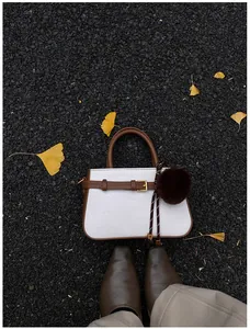 Detailed close-up of a white woven bucket bag with brown leather trim and fur ball charm