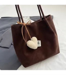Dettaglio della borsa tote in pelle scamosciata marrone con cuore di peluche e fiocco