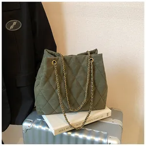 Detail van een olijfgroene gewatteerde tas met gouden kettingen op een koffer