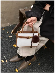 Detail of white woven bucket bag with brown leather trim and plush charm in autumn park