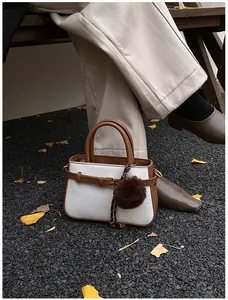 Detail of cream woven bucket bag with brown leather trim and plush pompom in autumn outdoor setting