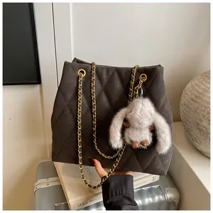 Detail van gewatteerde shopper met kettingriem en konijnenhanger op donker suède leer