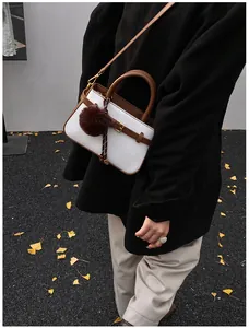 White woven bucket bag with brown leather trim and plush charm worn with a winter coat