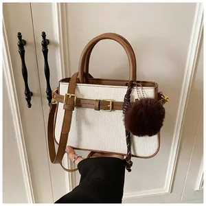 Detail of white woven bucket bag with brown leather trim and plush pom-pom charm decoration