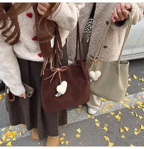 Detail of suede tote bag with plush heart charm and bow on ginkgo leaf background