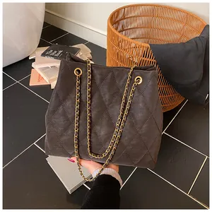 Detail van ruitstiksel en gouden ketting op de donkerbruine suède handtas voor dames