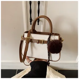 Detail of tweed bucket bag with brown leather handles and decorative fur pom-pom charm