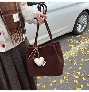 Detail of suede tote bag with white plush heart charm and autumn leaves on the ground