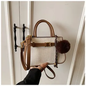 Close-up of woven bucket bag featuring brown leather trim and a dark plush ball pendant