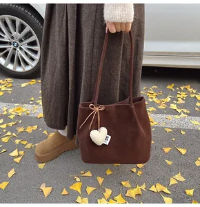 Detail of a brown suede tote bag featuring a plush white heart charm and a ribbon bow