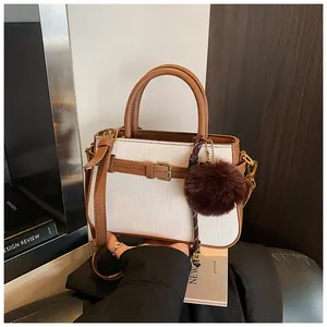 Detail of white woven bucket bag with brown leather trim and plush pompom charm