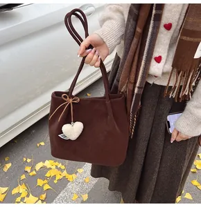 Detail of dark brown suede tote bag with plush heart pendant on autumn leaf background