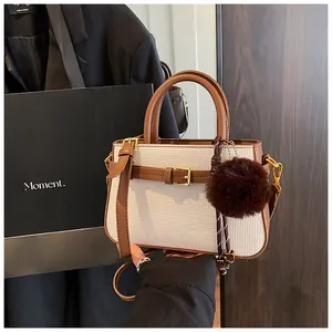 Detail of white woven bucket bag with brown leather trim, gold buckle, and fur ball charm