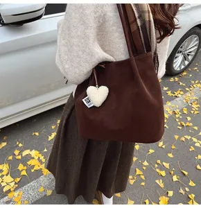 Detail of dark brown suede tote bag featuring a white fuzzy heart charm on shoulder