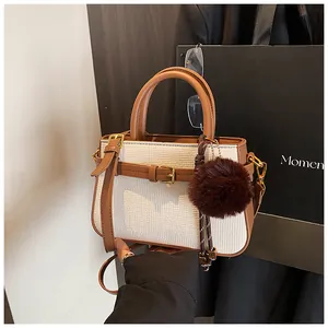 Detail of white woven bucket bag with brown leather trim and plush pompom charm