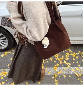 Detail of brown suede tote bag with heart plush charm against autumn city background