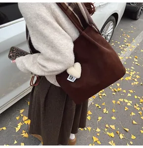 Detail view of large brown suede tote bag with plush heart charm and logo in autumn setting