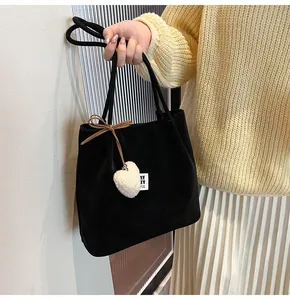 Detail of black suede tote bag featuring a brown bow tie and white plush heart charm