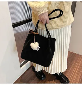 Detail of black suede tote bag with white plush heart charm on casual outfit