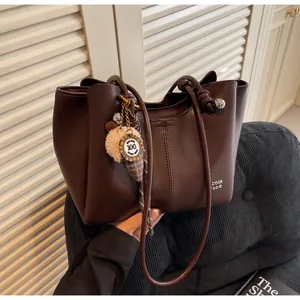 Detail of dark brown leather tote with silver sphere charm and decorative knot strap