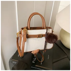 Close-up of two-tone bucket bag with woven texture, leather handle and fuzzy ball charm
