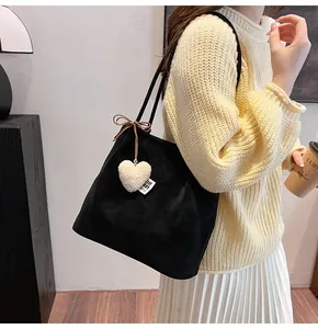 Close-up of black suede tote bag with a white heart plush charm and bow detail