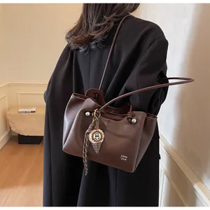 Detail of dark brown tote bag with white text branding and a cream charm pendant