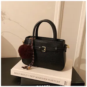 Detail of black textured bucket bag with gold buckle and fuzzy pom-pom charm decoration
