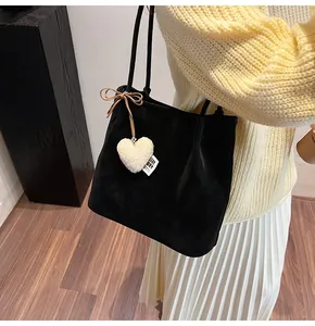 Detail of black suede tote bag with heart plush charm and bowknot on shoulder
