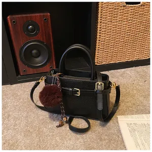 Detail of black textured bucket bag with golden hardware and plush pom-pom charm decoration