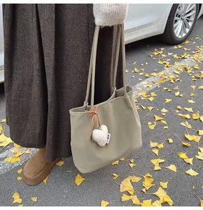 Close-up of suede tote bag with heart plush charm against autumn ginkgo leaves background