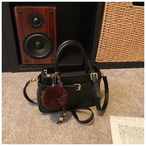 Detail of black bucket bag with gold buckle, textured leather and plush ball charm
