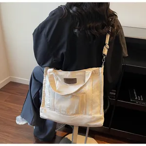 Detail view of a cream canvas tote bag with adjustable shoulder strap and leather patch