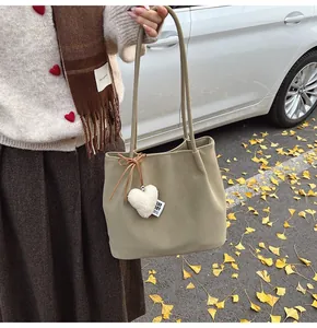 Chic beige faux suede tote bag with plush heart charm and bow in an autumn street setting