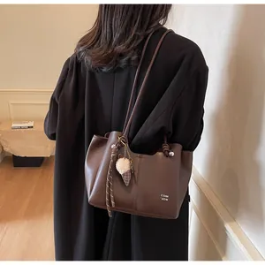 Detail of dark brown tote bag with white lettering and plush charm on a shoulder strap