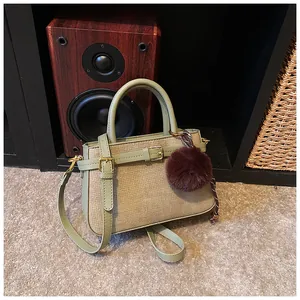 Close-up of sage green woven bucket bag with PU handles and brown fur pom-pom detail