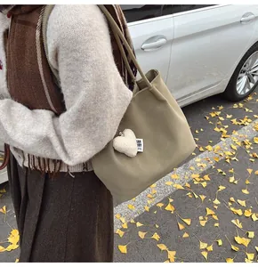 Close-up of beige suede tote bag with heart charm against autumn leaves background