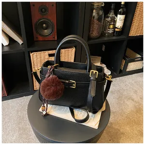Detail of woven texture black bucket bag with brown pompom and gold buckle accents